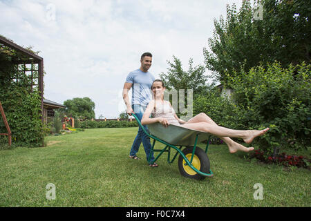 Man pushing girlfriend in wheelbarrow at backyard Stock Photo