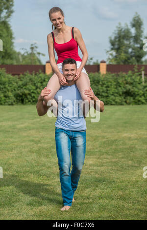 Full length portrait of happy young man carrying woman on shoulders in backyard Stock Photo