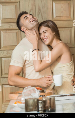 Cheerful young couple embracing in kitchen Stock Photo