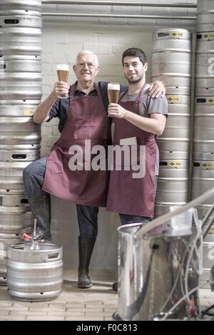 Two brewers drinking beer in the brewery, next to kegs Stock Photo