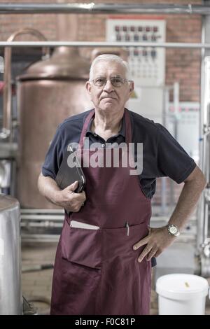 Portrait of brewer in brewery, standing next to stainless steel tanks Stock Photo