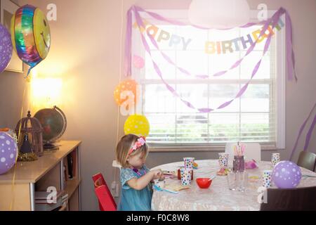 Portrait of blonde girl sitting at birthday party table Stock Photo