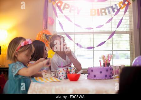 Three children sitting at table eating purple birthday cake Stock Photo