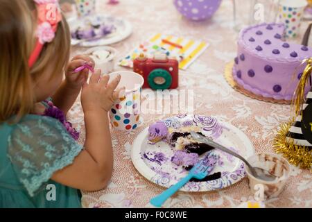 Side view of of girl sitting at birthday party table eating purple cake Stock Photo