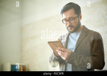 Young Asian businessman making notes in notepad Stock Photo