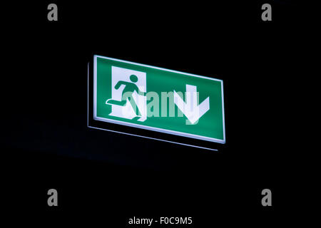 Exit sign hanging on the ceiling of a parking garage. In the dark illuminated green and white symbol. Stock Photo