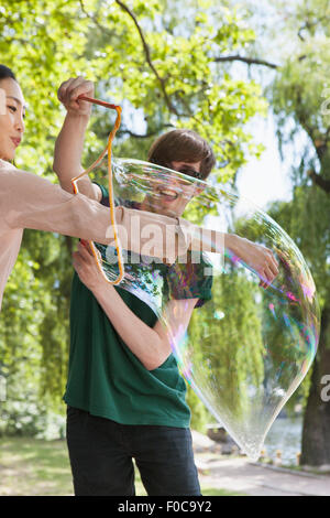Happy man putting friend's hand in big bubble at park Stock Photo