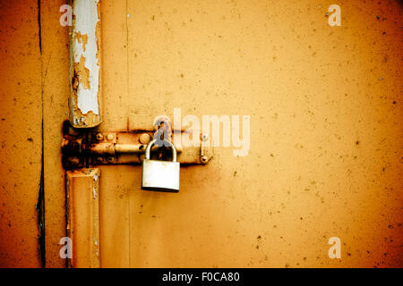 Rusty padlock on old orange painted wooden door Stock Photo