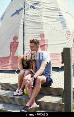 Happy young couple sitting on teepee structure while glamping Stock Photo