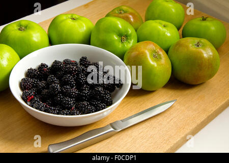 Bramley's Apples with Blackberries in white bowl with knife on wooden chopping board Stock Photo