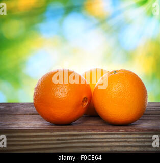 Oranges on wooden table over shiny leaves background Stock Photo