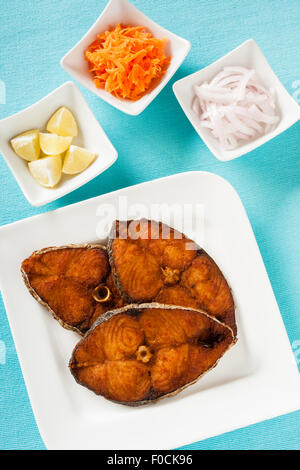 Overhead view of delicious Indian seer (mackerel) fish fillets fry served with shredded carrots, raw onion rings, lemon. Stock Photo