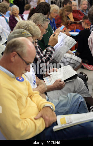 People sitting in audience on rows of chairs reading while waiting for event Stock Photo