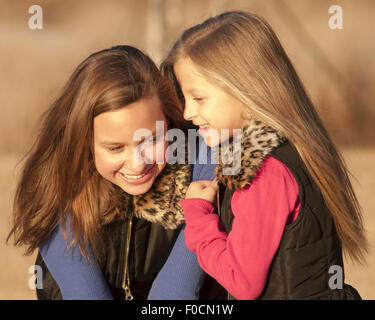 two sisters/friends telling secrets outside.  It is fall weather. Sweet light. Stock Photo
