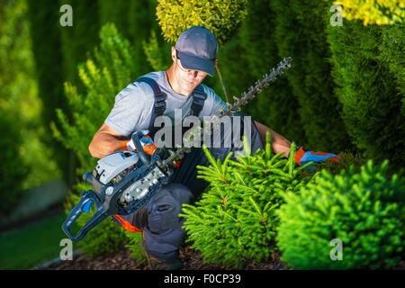 Trimming Works in a Garden. Professional Gardener with His Pro Garden Equipment During His Work. Gasoline Plants Trimmer Equipme Stock Photo