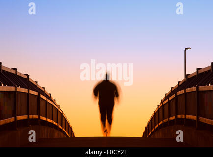 Wide foot bridge and male jogger during daybreak. Jogger has motion blur effect. Stock Photo