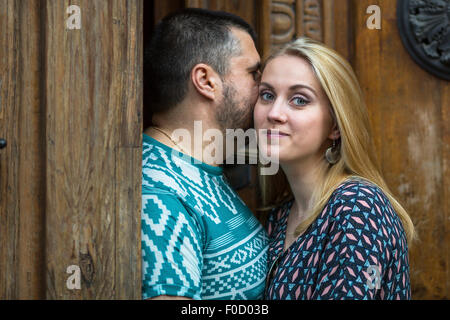 Couple standing, man whispers to the young woman, she looks into the camera. Stock Photo