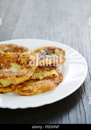 Fresh fried zucchini potato pancakes on a white plate on the wooden table. Stock Photo