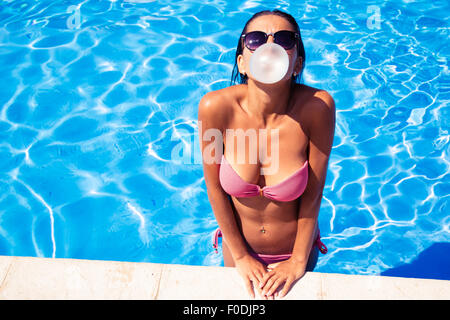Beautiful woman blowing bubble with gum in swim pool outdoors Stock Photo