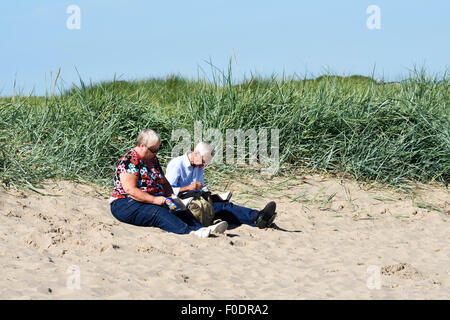 Older couple sitting fully dressed on the sandy beach in Fleetwood, Lancashire, UK Stock Photo