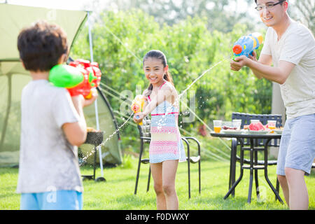 Happy father and children playing squirt guns Stock Photo