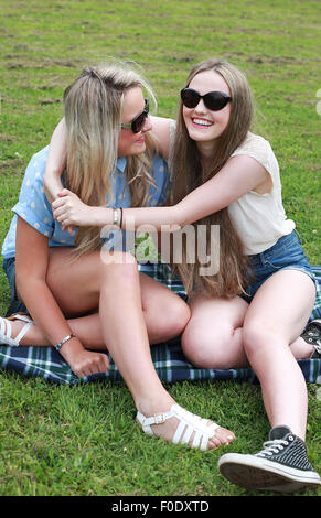Two teenage girls sitting on the grass in summer time laughing Stock Photo