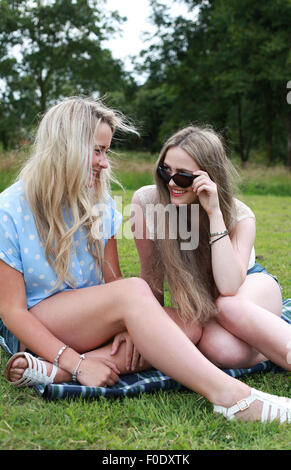 Two teenage girls sitting on the grass in summer time laughing