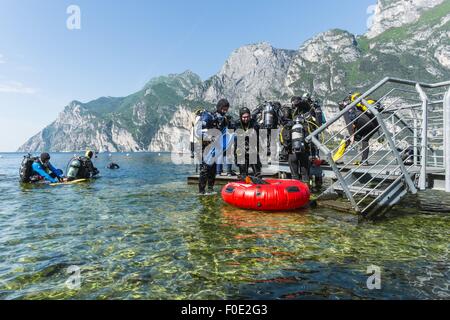 Scuba divers getting ready for immersion at Lake Garda, preparing their gear and putting on the fins. Stock Photo
