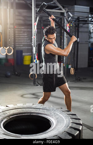 Young man hammering large tire at gym Stock Photo