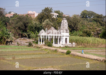 India; road from Udaipur to Jodhpur. A small roadside Hindu temple with a girl in school uniform in fields. Stock Photo