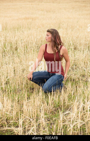 Young woman posing in large wheat field wearing red tank top and jeans. Stock Photo