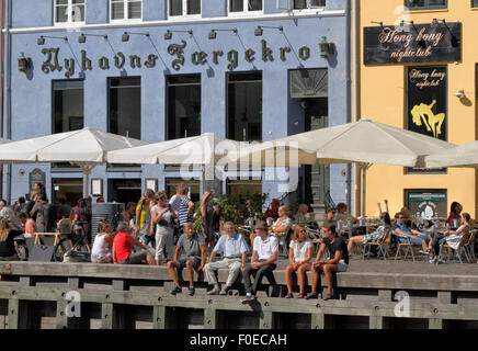 People meet and talk over a drink in the sun in the cosy ambience in charming Nyhavn. Many prefer to sit on the wharf among the old  ships. Hygge. Stock Photo