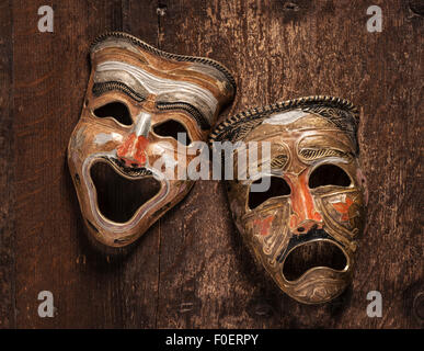 Comedy and tragedy masks lying on wooden background. Still life showing emotion through the contrast of happiness and sadness. Stock Photo