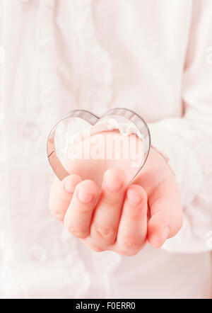 Little girl holding heart shaped cookie cutter in her hand. Conceptual image of childhood, love and affection. Stock Photo