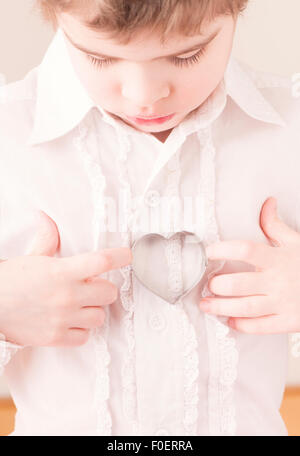 Little girl holding heart shaped cookie cutter in her hands. Conceptual image of childhood, love and affection. Stock Photo