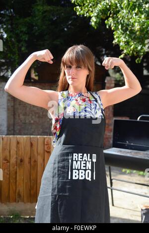 Attractive young woman showing female strength wearing a barbecue apron outdoors Stock Photo