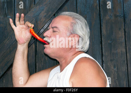 Young caucasian man with a red hot chili pepper in his mouth Stock Photo