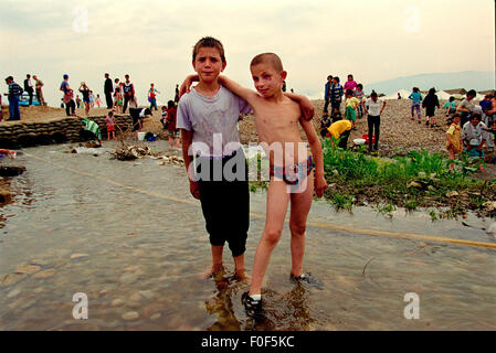 Kosovan refugees at camp Strankovic Macedonia 1999 , to young boys play in the stream that runs through the camp while other people wash clothes Stock Photo