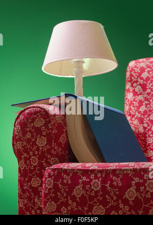 Book on red armchair rest left after reading, with green background and pink lamp illuminating the scene. Stock Photo