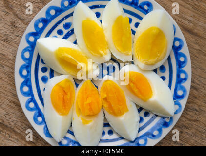 Two colors yolk, sliced hard boiled eggs in a blue decorated plate on wooden kitchen table. Stock Photo