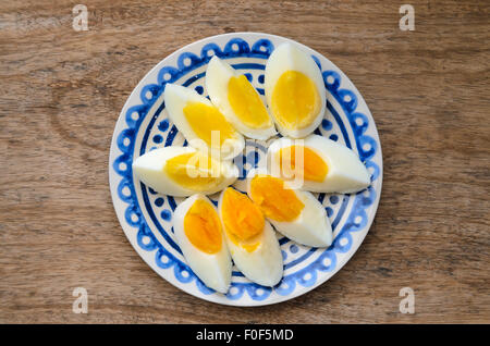Two colors yolk, sliced hard boiled eggs in a blue decorated plate on wooden kitchen table. Stock Photo