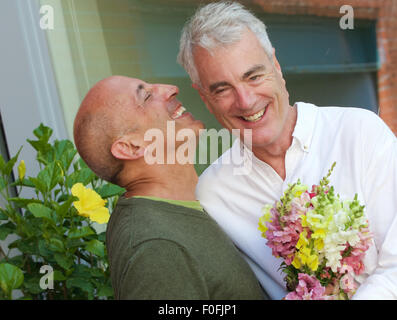 Older, mature, senior gay male couple, smiling and exchanging bouquet of flowers to celebrate happy occasion such as engagement Stock Photo