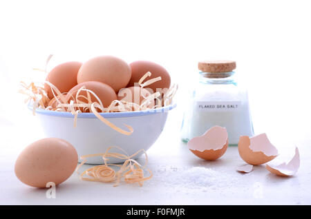 Farm fresh eggs in vintage bowl with broken egg shells and salt on vintage white wood table. Stock Photo