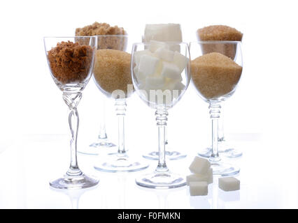 Different types of sugar including white, brown, dark brown, demerara, coffee sugar crystals and sugar cubes, displayed in glass Stock Photo
