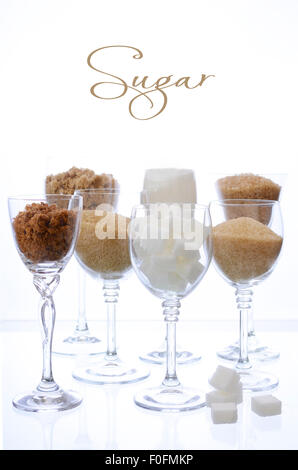 Different types of sugar including white, brown, dark brown, demerara, coffee sugar crystals and sugar cubes, displayed in glass Stock Photo
