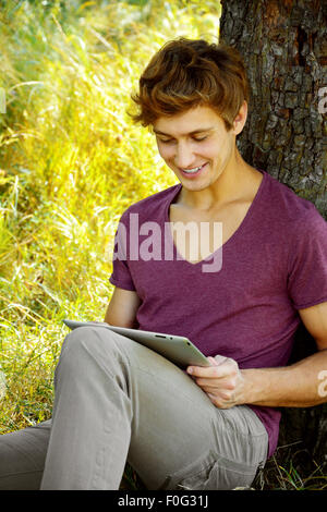 Young man is using tablet near the tree Stock Photo