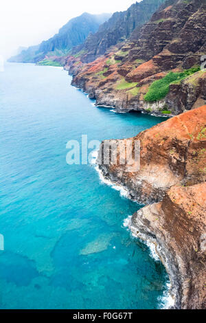 An aerial view of the Na Pali coast in Kauai Hawaii during a vibrant, sunny day shows the rich colors of the scenic coastline. Stock Photo