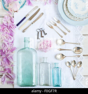 a collection of vintage bottles,  cutlery, plates, old keys, and peonies Stock Photo
