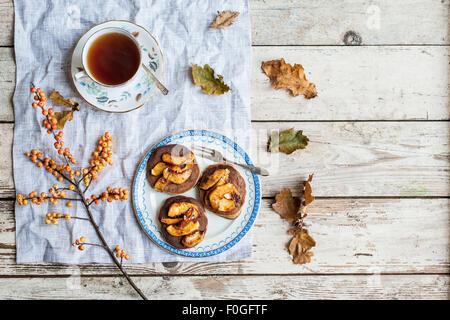 pancakes with caramelised apples on vintage plate, with tea in vintage teacup, oak leaves and ilex berries Stock Photo