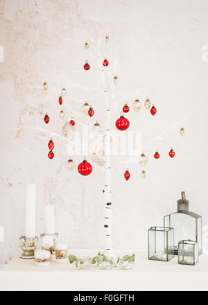 Christmas decorations at home - birch Christmas tree, candles, lanterns, silver and red mercury glass baubles, tealights Stock Photo